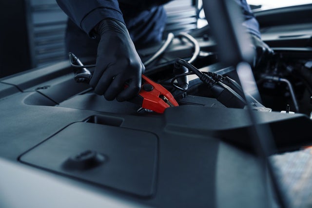 Service technician applying cables to a car battery under the hood of a vehicle