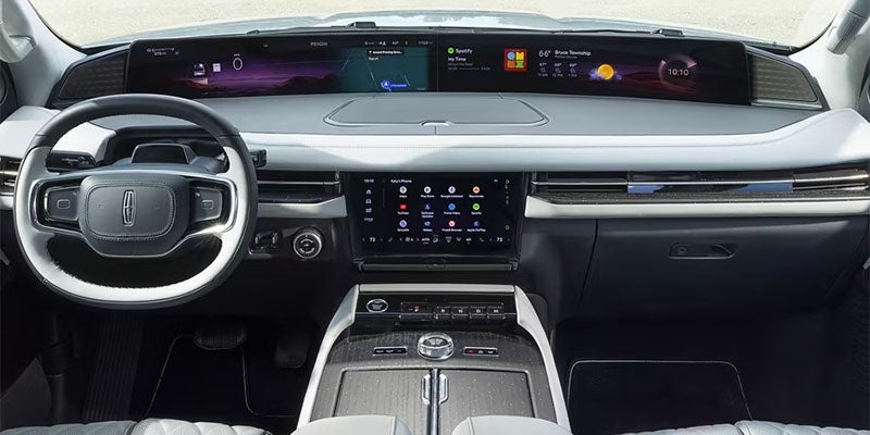 A modern car dashboard with a panoramic digital display and a large central touchscreen, a black and white steering wheel.