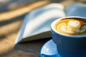A hot latte with a book in the background.