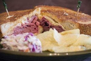 A corn beef sandwich with potato chips and coleslaw. 