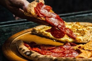 A hand grabbing a slice of pepperoni pizza.