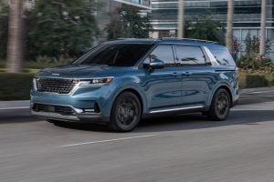A light blue metallic 2022 Kia Carnival driving in the city.