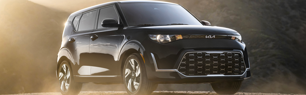 Kia Soul SUV driving on a scenic road with mountain backdrop.