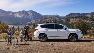 A mother with her son and daughter on their bikes outside near a lake with the mountains in the background. Standing by a white 2022 Hyundai Santa Scruz.