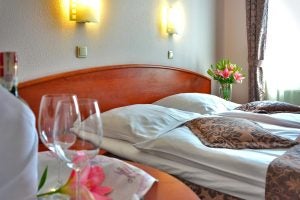 Inside of a hotel room with wine glasses and flowers with the bed in the background.