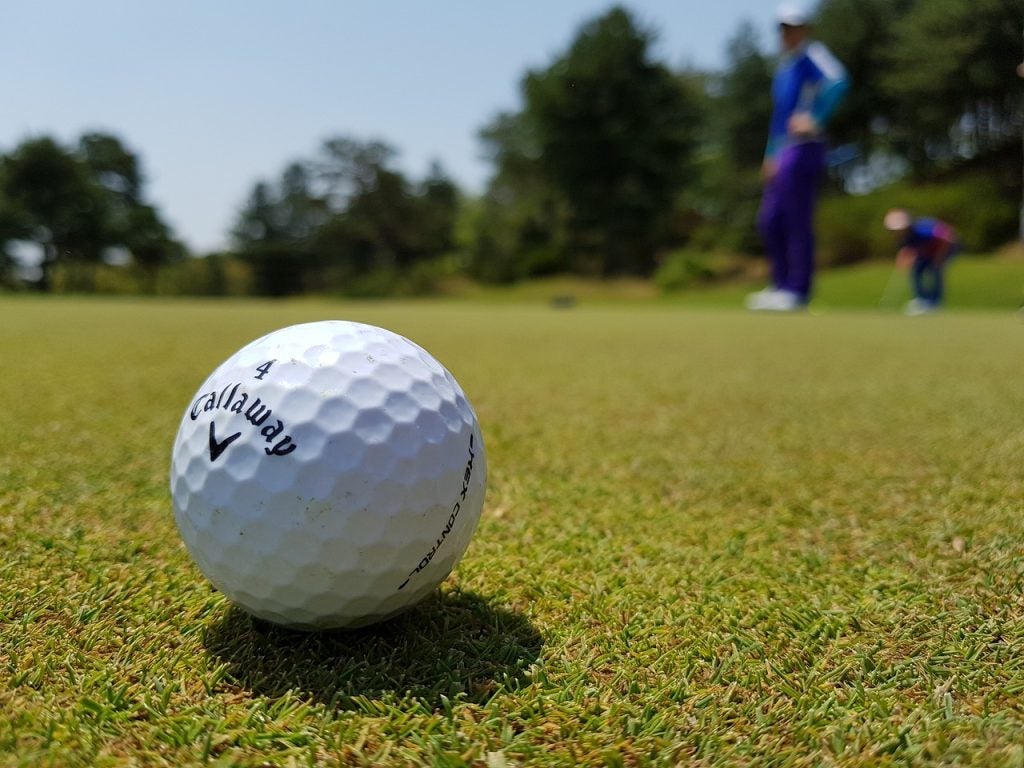 A golf ball and someone that just hit it in the background.