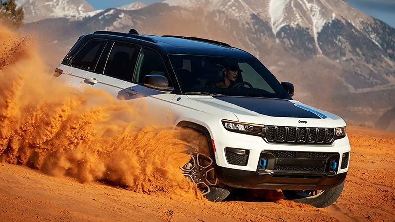 A white 2023 Jeep Grand Cherokee driving through the desert.