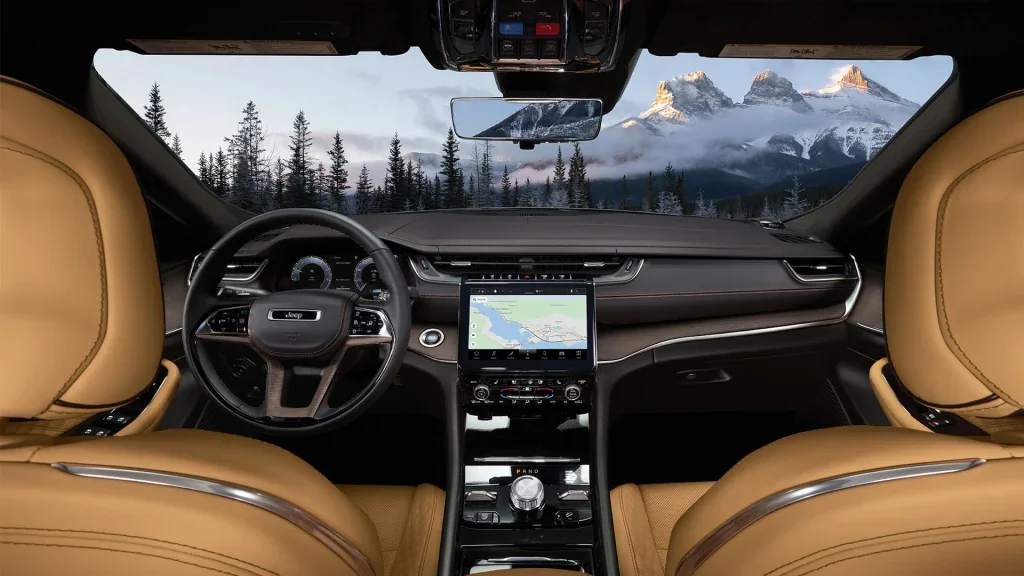 The interior of a Jeep SUV, featuring tan leather seats, a dashboard with a large touchscreen displaying a map, and a scenic mountain view through the windshield.