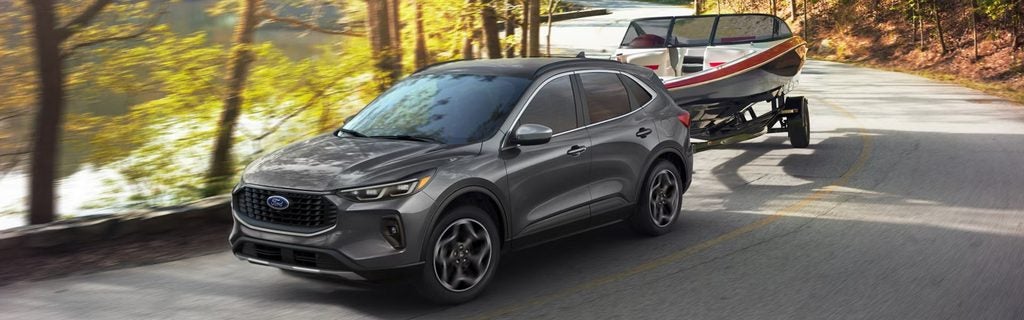 Gray Ford SUV towing a boat trailer along a wooded road.