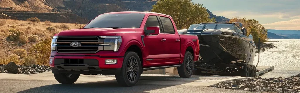 Red Ford F-150 towing a boat onto a lakeside ramp.