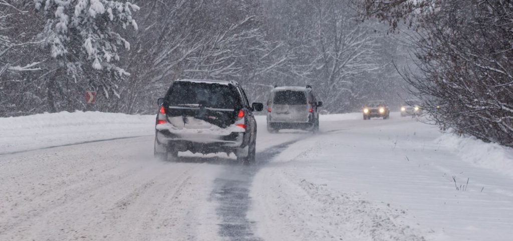 Vehicles driving on very snowy roads during a snow storm.
