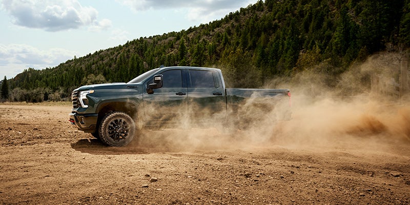 A Chevrolet Silverado truck kicking up dust as it drives off-road through a rugged terrain.