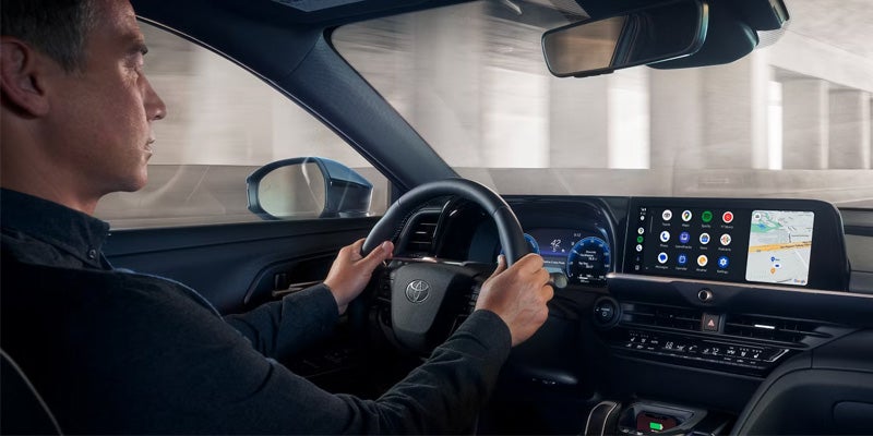 Driver using Toyota vehicle dashboard with digital display and infotainment screen.