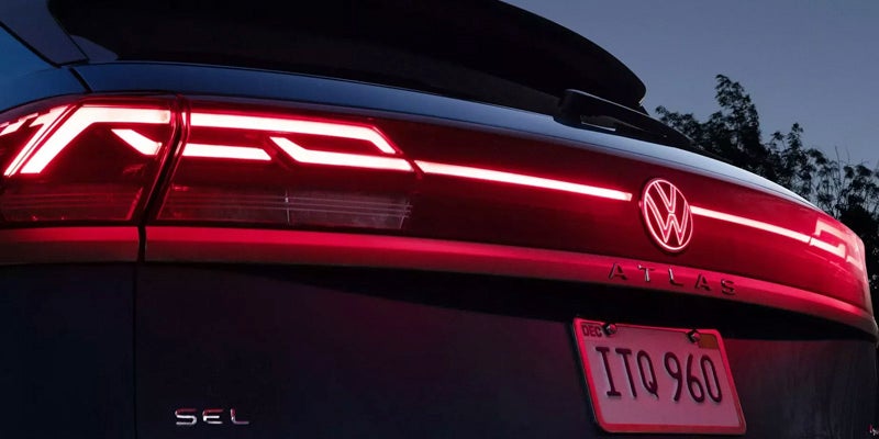 Rear view of a 2026 Volkswagen Atlas showing illuminated LED taillights, VW badge, Atlas lettering, and a visible license plate at dusk.