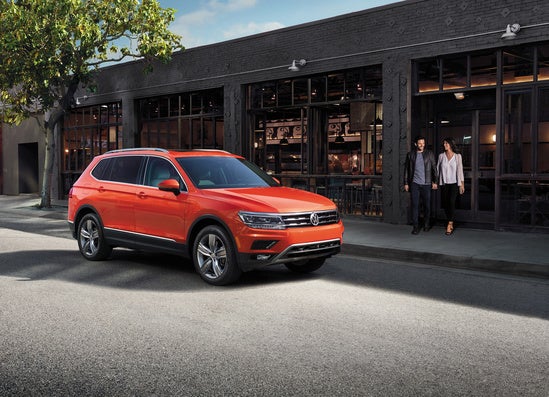 orange Volkswagen Tiguan parked in front of a shop downtown