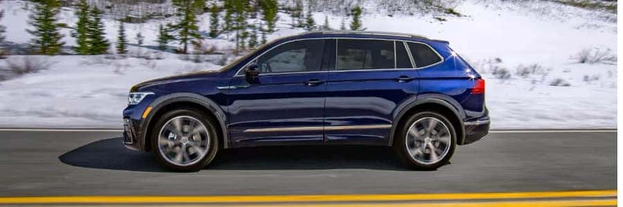 an atlantic blue tiguan drives on a road in a snowy environment