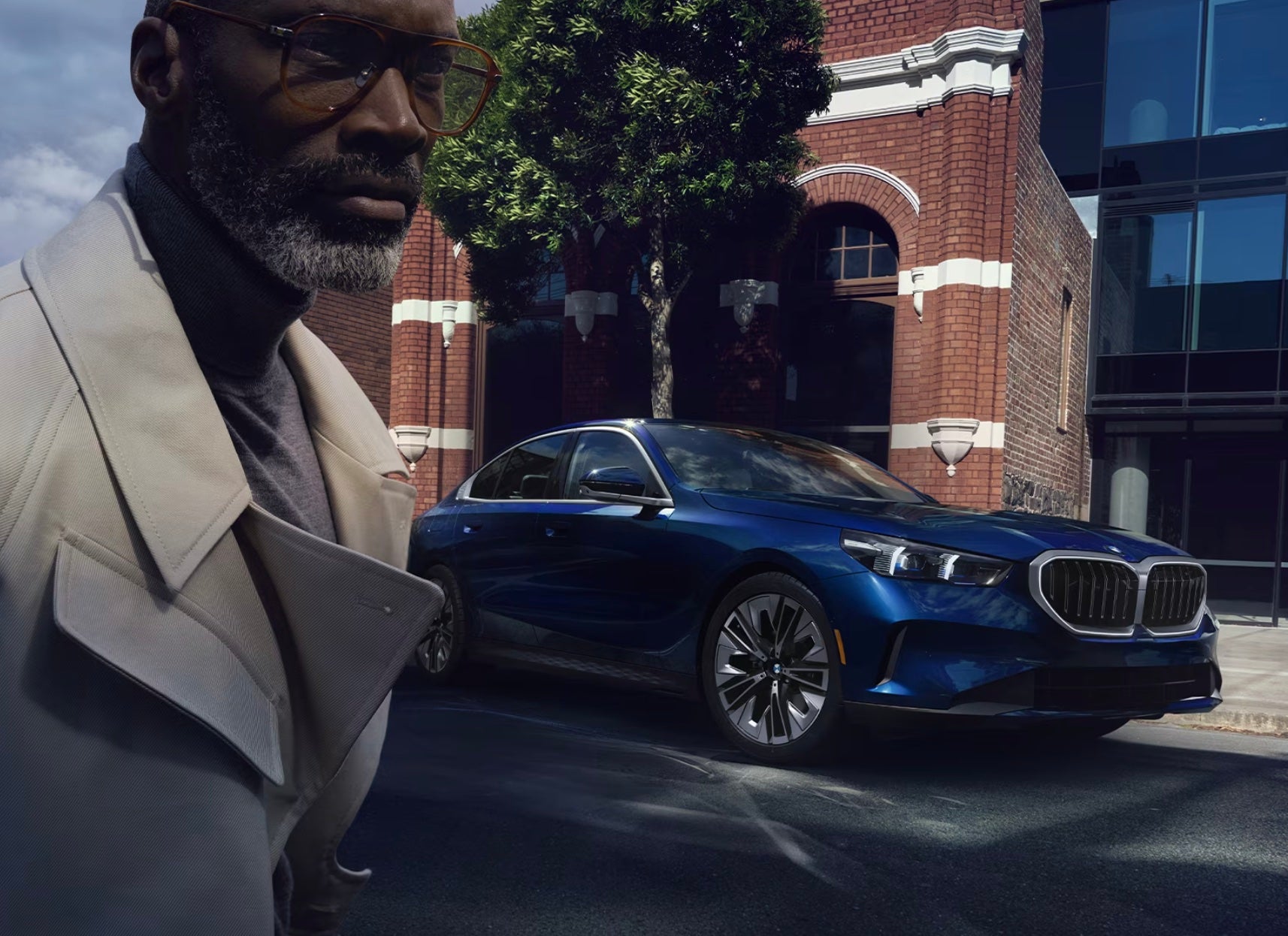 Man walking past a blue BMW X5 Series in the city with shadowy light from the sun beaming down on both himself and the BMW sedan