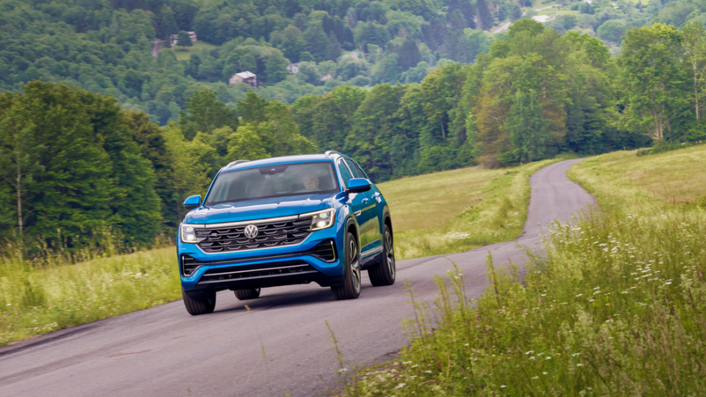 2026 Volkswagen Atlas Cross Sport SUV driving through scenic countryside road with bold blue paint.