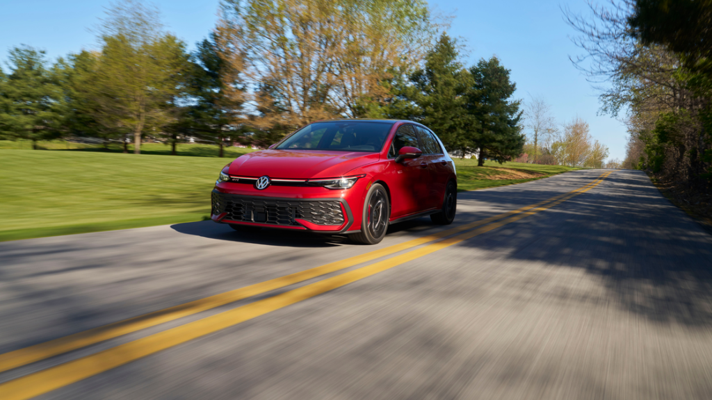 Front-side view of a red 2025 Volkswagen Golf GTI in motion on a tree-lined two-lane road.