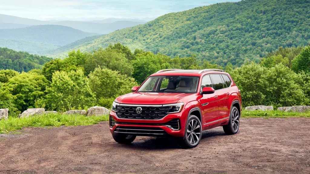 2025 Volkswagen Atlas SUV in red parked at a mountain overlook, showcasing bold grille design, alloy wheels, and spacious three-row exterior styling.