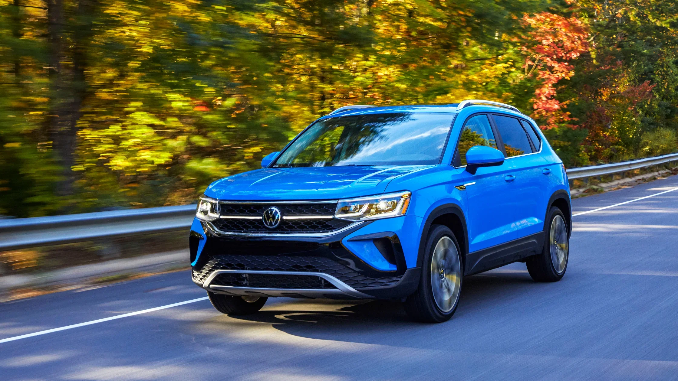 2024 Volkswagen Taos in striking blue driving through colorful autumn scenery.