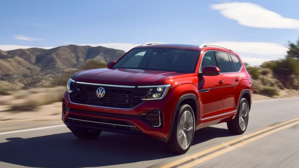 2026 Volkswagen Atlas SUV driving on an open highway, highlighting updated front fascia, LED headlights, roof rails, and refined midsize SUV proportions.