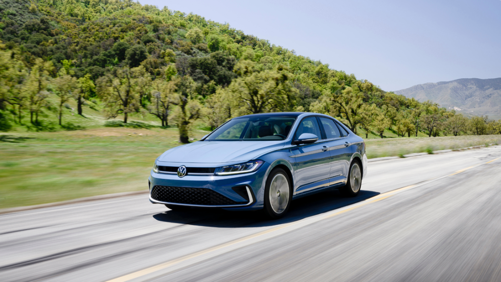 2025 Volkswagen Jetta driving on a sunny open highway with rolling green hills and clear mountain views.