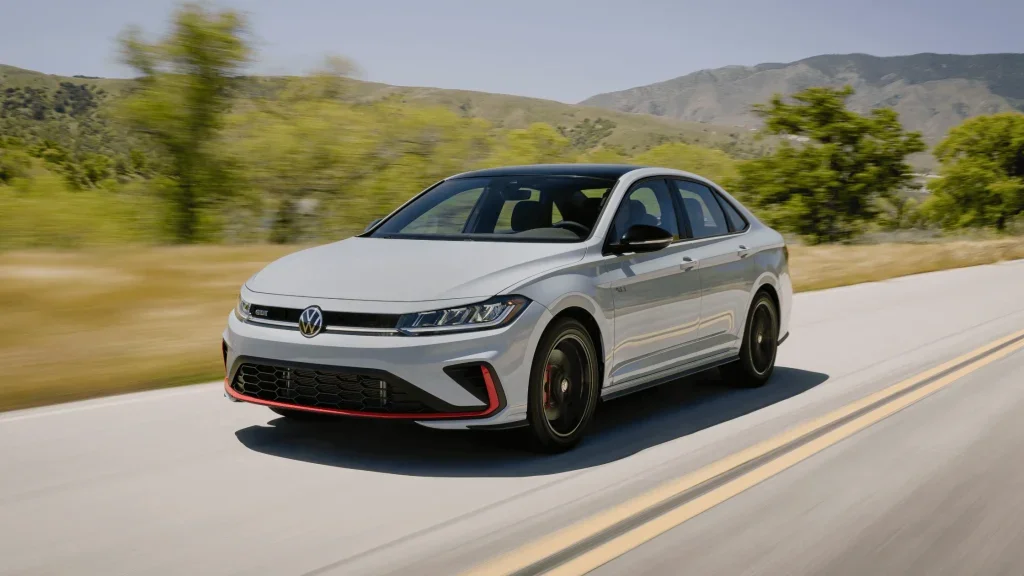 2026 Volkswagen Jetta GLI in white shown on a highway with sporty red trim accents and black alloy wheels.