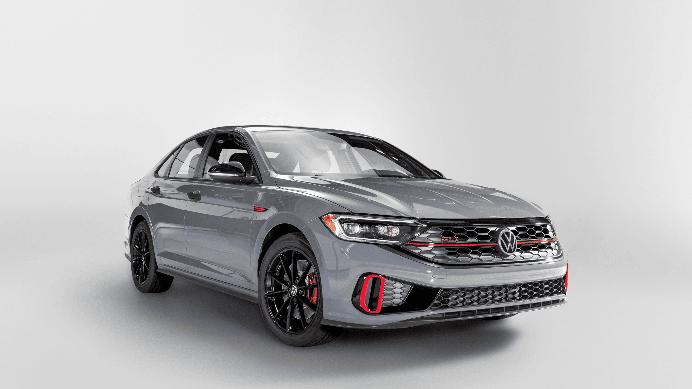2024 Volkswagen Jetta GLI in sleek gray with black and red accents, parked in a minimalist studio setting, showcasing its sporty grille, distinctive headlights, and modern design.
