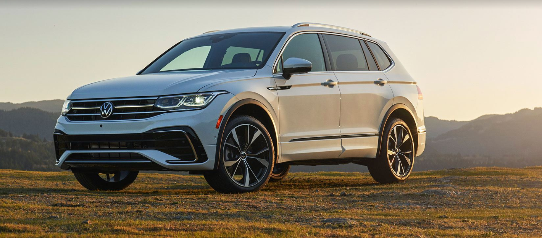 2022 Tiguan parked in a field with the sun shining down and a mountain range in the background.