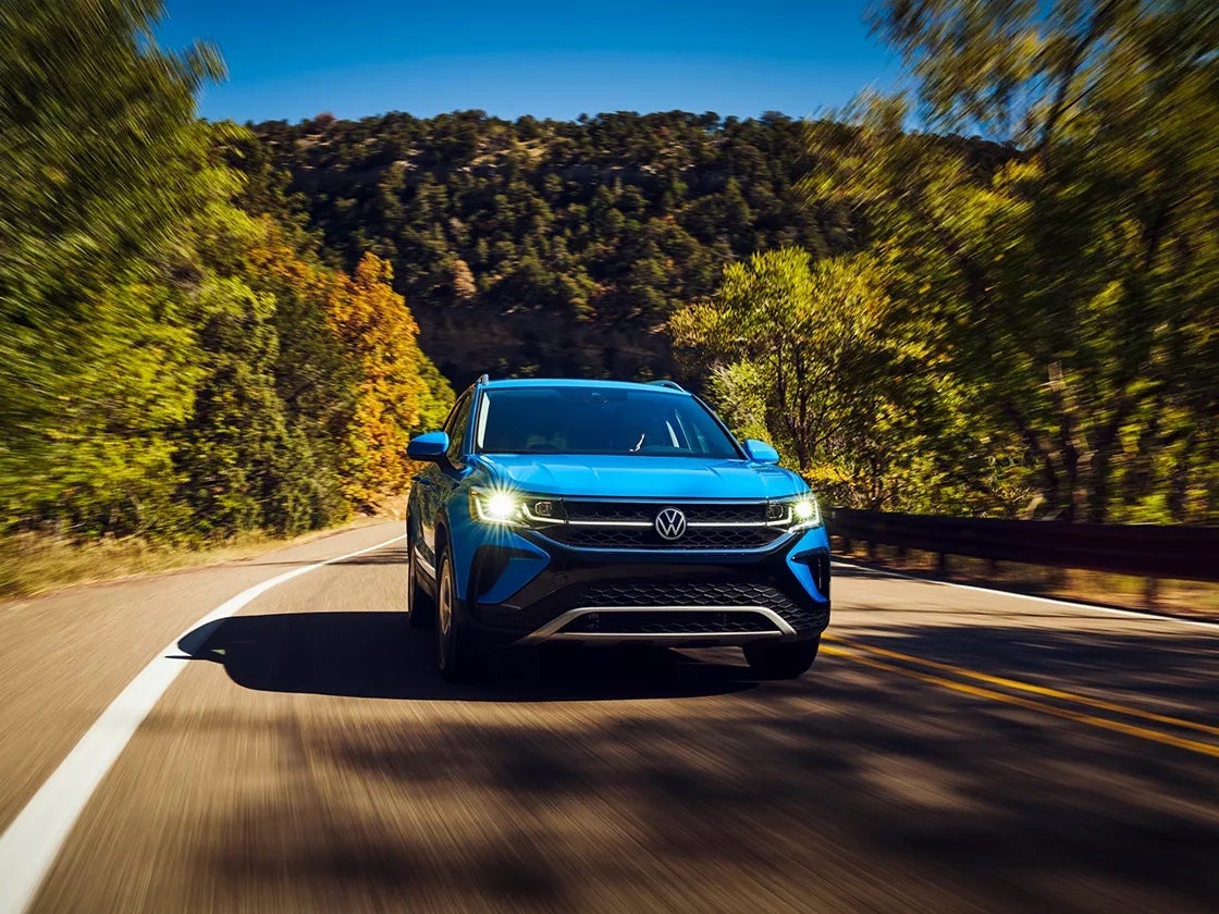 Blue 2023 Volkswagen Taos driving down a forested road