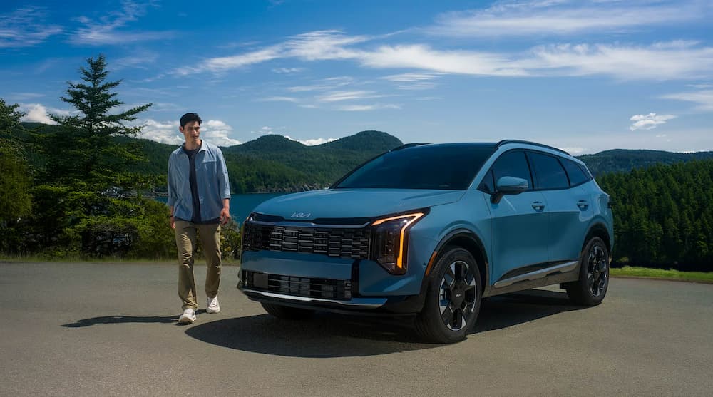 A blue 2026 Kia Sportage Hybrid parked near a person walking.