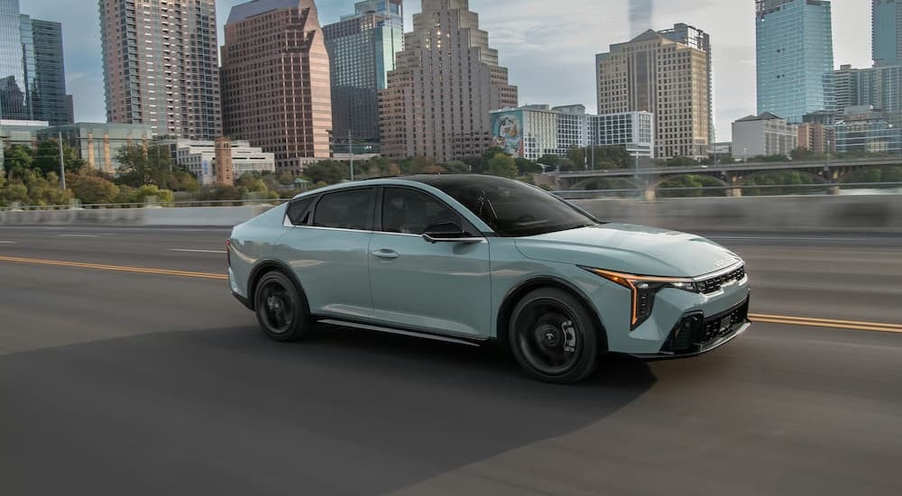 A light blue 2026 Kia K4 driving near a city.