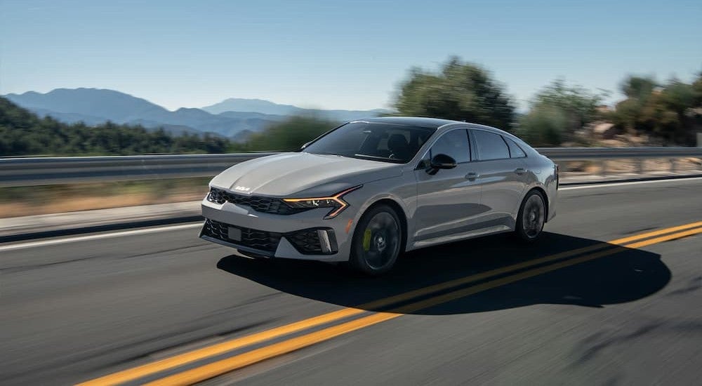 A gray 2026 Kia K5 driving on a highway.