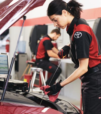 A Toyota service technician checking the oil level on a red Toyota car