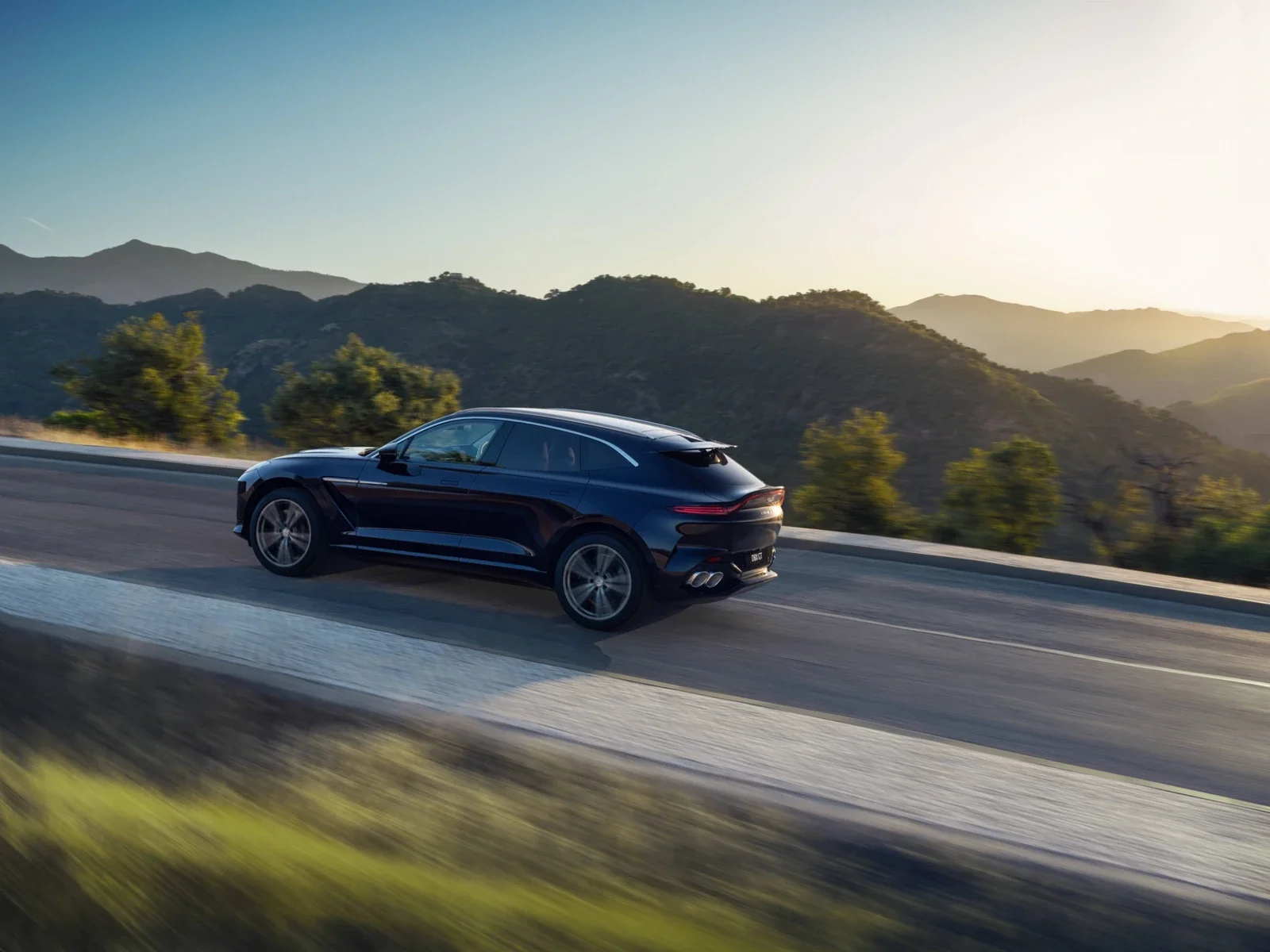 Aston Martin DBX GT driving along a mountain road at sunset