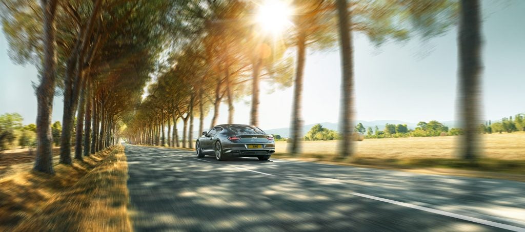 Bentley Continental GT on tree-lined road driving away from camera.