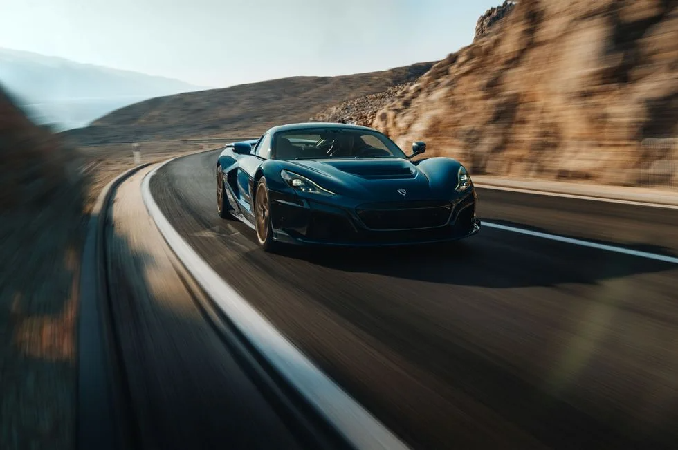 Blue Rimac Nevera on a winding coastal road.