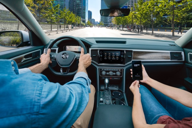 VW Atlas interior with man holding steering wheel and woman connecting a smart phone to the infotainment system
