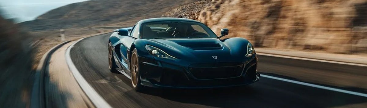 Blue Rimac Nevera on a winding coastal road.