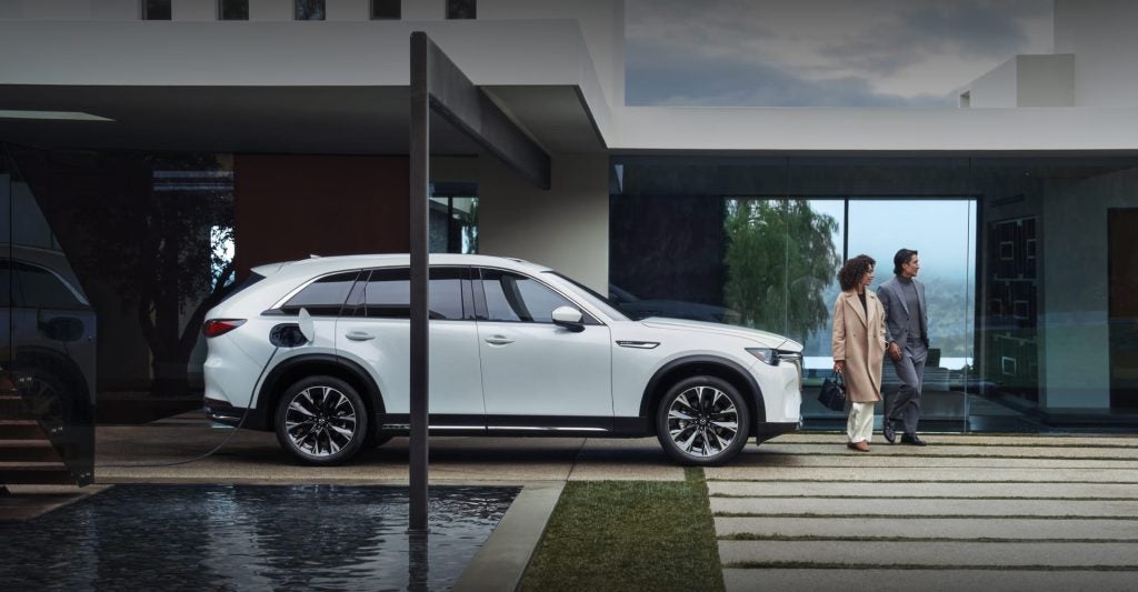 A white SUV charging outside a house with a couple walking.