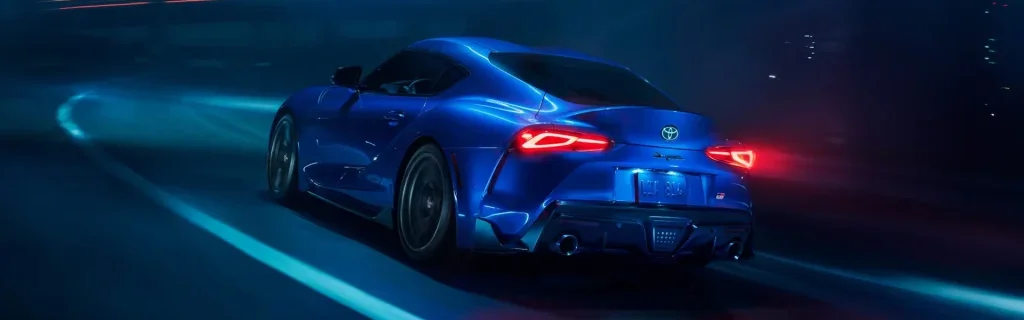 Blue Toyota GR Supra sports car driving on a neon-lit night road.