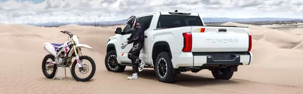 White Toyota Tundra pickup parked in desert beside dirt bike and rider.
