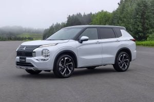 White Mitsubishi Outlander PHEV parked on paved road near forest in misty weather
