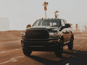 Black RAM Truck driving through sand covered streets with palm trees in the background. 