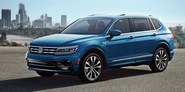 side view of a blue 2020 Volkswagen Tiguan parked with city skyline in background