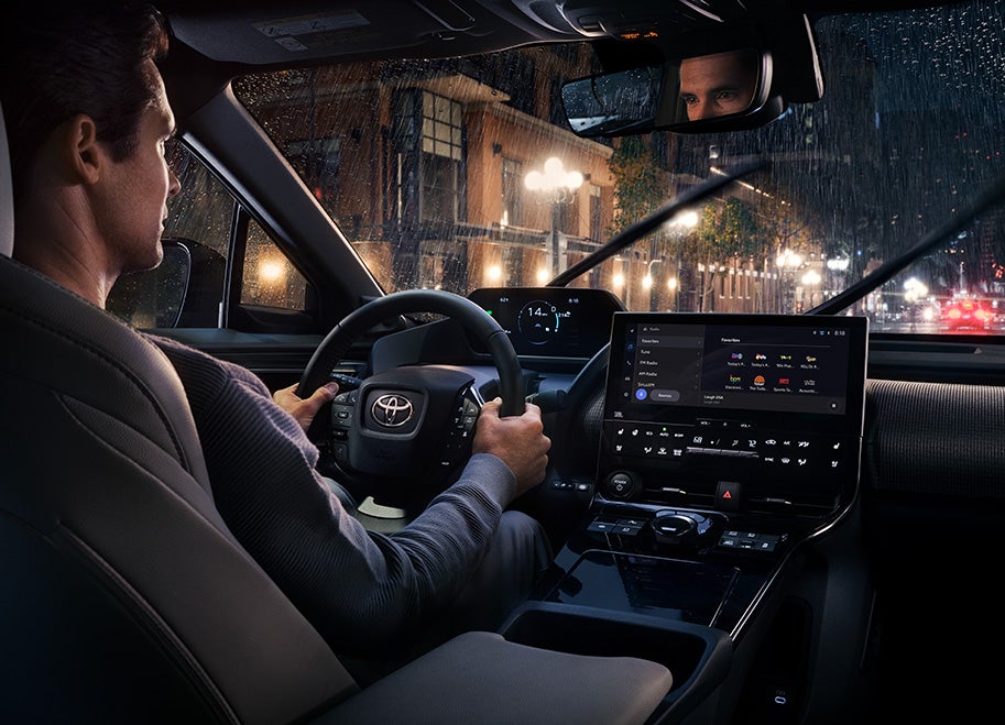 The All-New Toyota Electric Car: The Toyota bZ4X BEV at Bennett Toyota of Lebanon | Man Driving Toyota bZ4X BEV on a Rainy Night - Featuring Interior Design Including Large Infotainment System & Digital Gauge Cluster