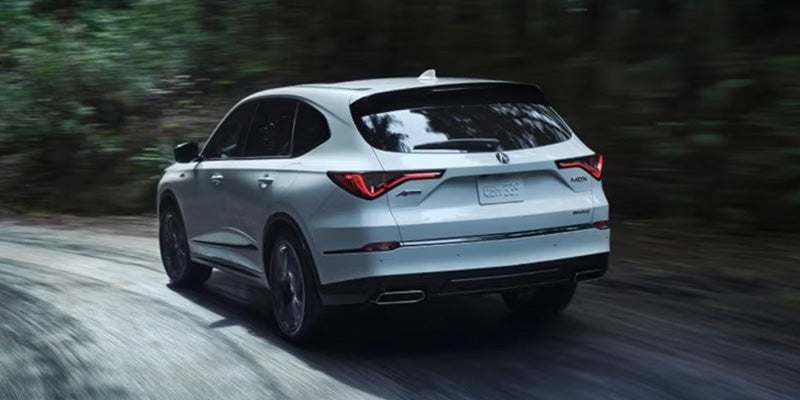 White Acura MDX driving on a forest road from rear angle