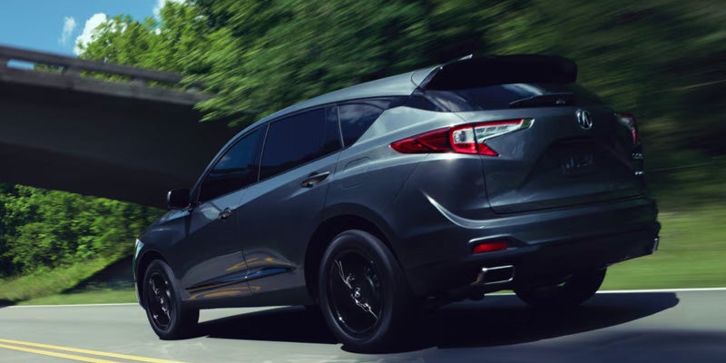 Dark gray SUV driving at speed on a road under a bridge with motion blur and greenery in the background.