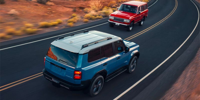 A 2025 Toyota Land Cruiser driving past a vintage Toyota Land Cruiser